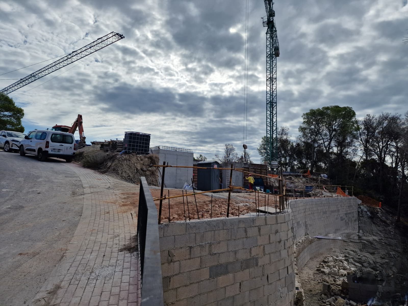 Construction progress showing the curved retaining walls, paved access road, and heavy machinery on-site for the initial structural phase in Moraira.
