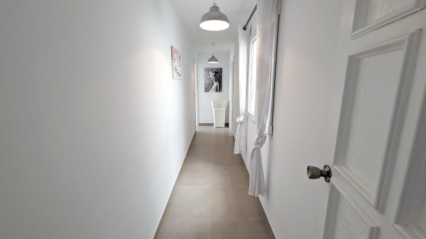 Bright hallway featuring white walls, porcelain floor tiles, industrial-style pendant lighting, and windows with white knotted curtains.