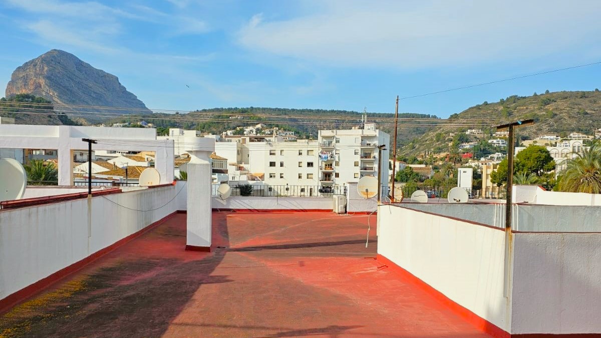 Communal roof terrace featuring red flooring and white perimeter walls, offering panoramic views of the Montgó mountain and surrounding Javea landscape.