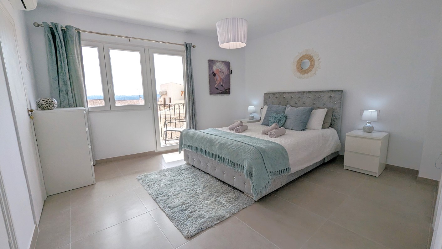 Master bedroom featuring a tufted headboard, private terrace access via glass doors, and integrated storage with white bedside tables.