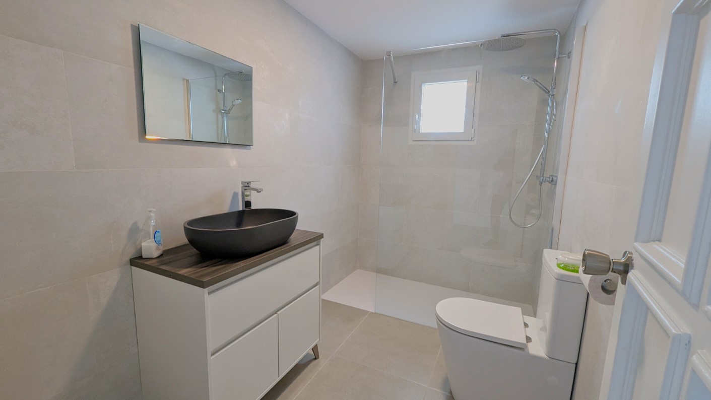 Modern bathroom featuring a black vessel sink on a white vanity, a walk-in shower with a glass screen, and large-format grey tiles.