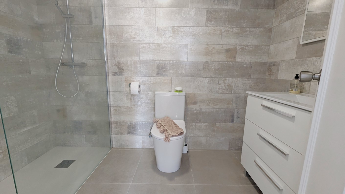 Modern bathroom featuring a walk-in shower with glass partition, textured grey wall tiles, and a white vanity unit with integrated storage.