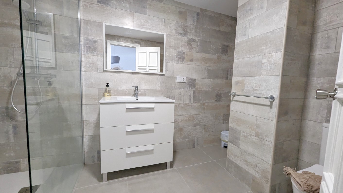 Modern bathroom featuring a white three-drawer vanity, a walk-in shower with a glass screen, and elegant textured ceramic wall tiling in neutral tones.