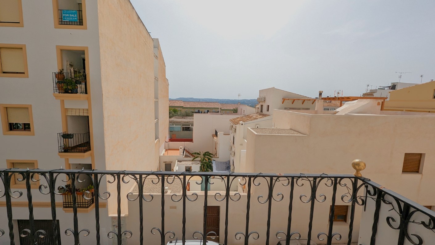 View from the balcony with a wrought iron railing, looking out over the urban landscape of Javea Old Town towards the distant mountain horizon.