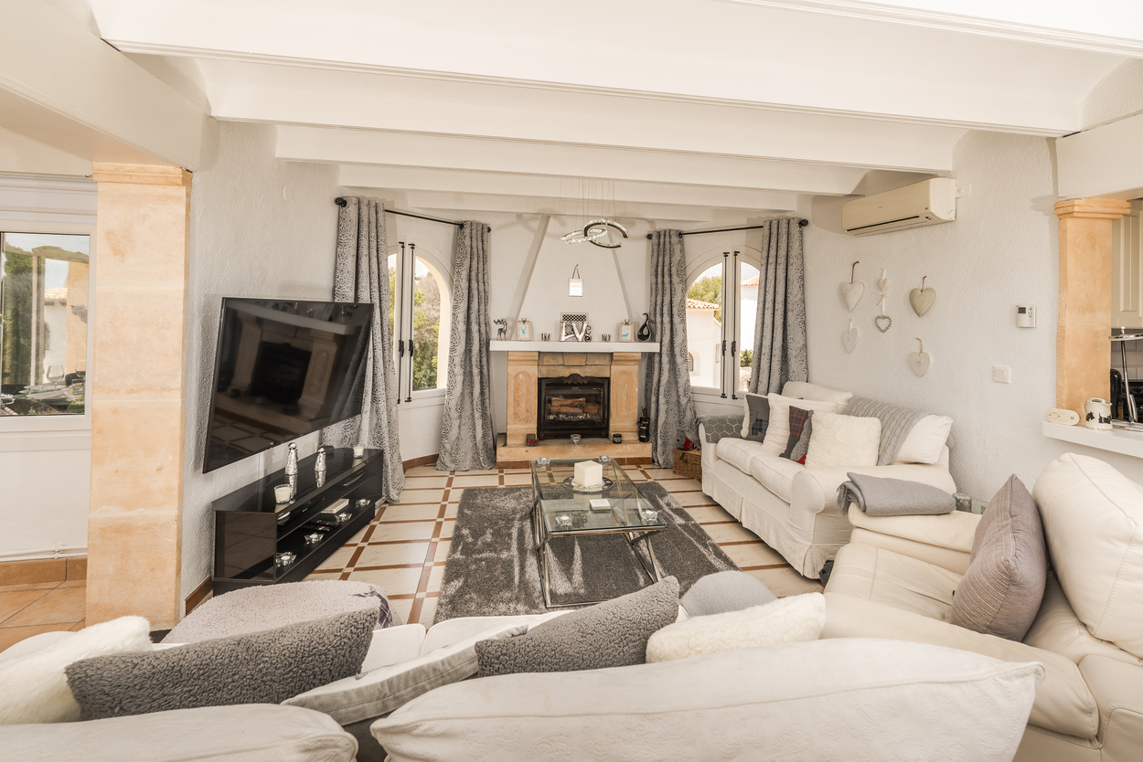 Bright living room featuring a natural Tosca stone fireplace, white beamed ceilings, stone pillars, and traditional tiled flooring.
