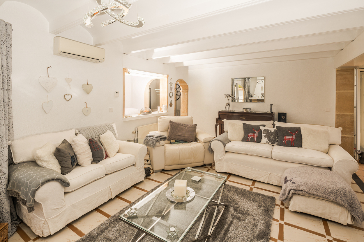 Bright living room featuring white beamed ceilings, comfortable seating, a glass coffee table, and an original Tosca stone archway leading to other areas.