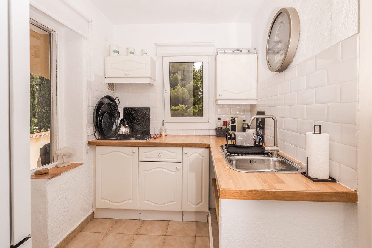 Compact kitchen featuring white cabinetry, wooden countertops, and a subway tile backsplash. It includes a gas hob, stainless steel sink, and garden views through the window.