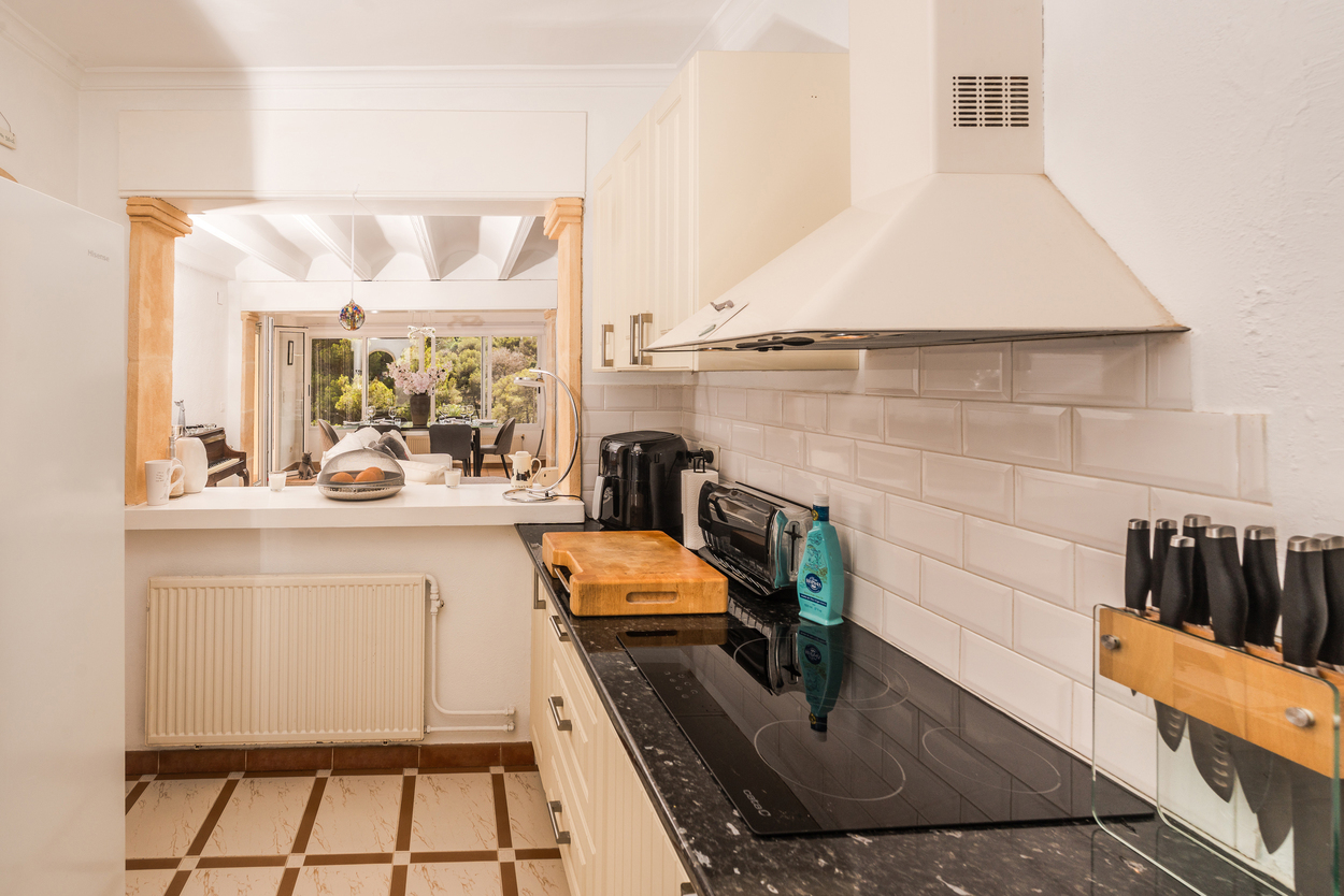 Equipped kitchen featuring dark granite countertops, subway tiles, and a breakfast bar opening into the living area through traditional tosca stone pillars.