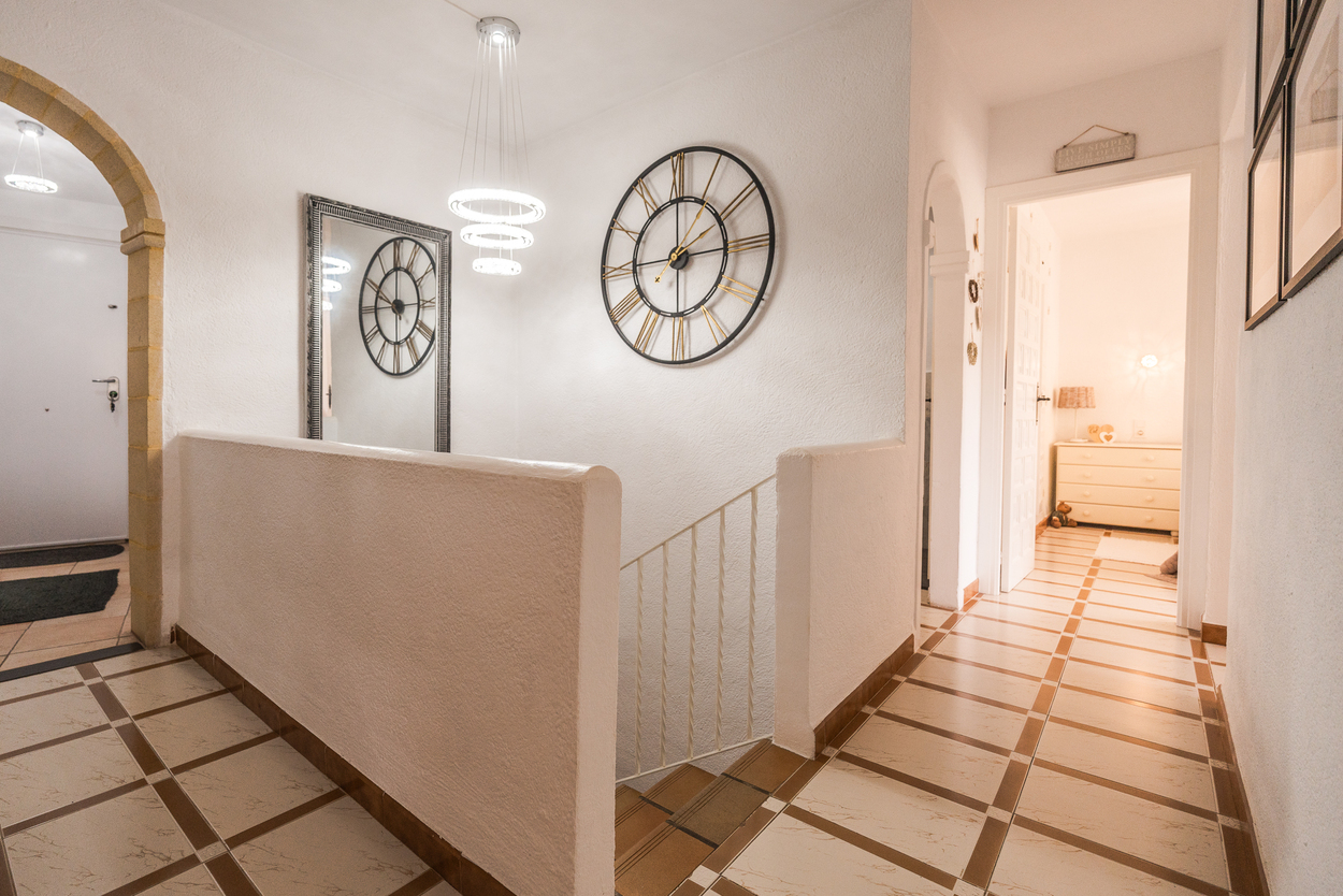 Hallway landing featuring a traditional Tosca stone arch, tiled flooring with geometric patterns, and a modern LED ring chandelier over the central staircase.
