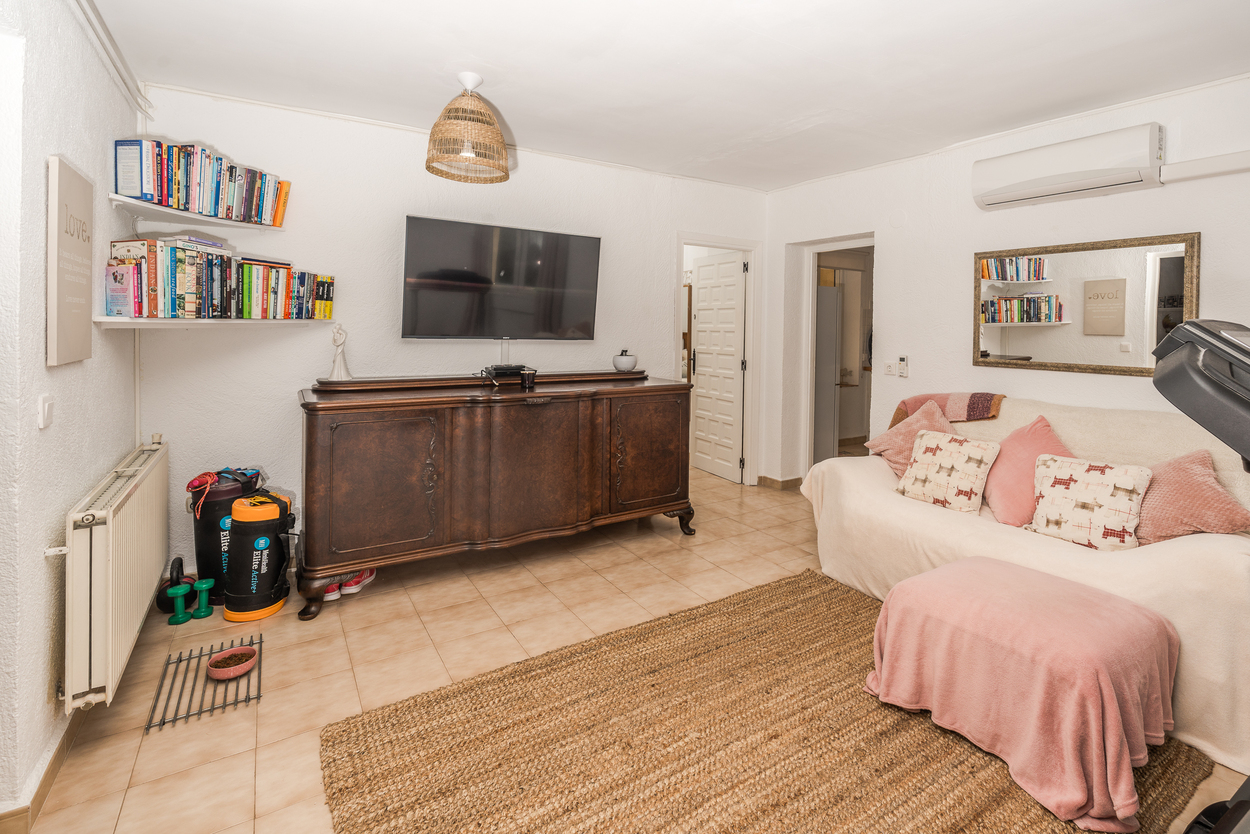 Living area featuring a large wooden sideboard, wall-mounted TV, and tiled floors. Includes gas central heating, air conditioning, and a natural fiber rug.