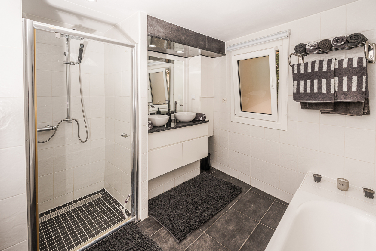 Modern bathroom featuring a walk-in glass shower, double vessel sinks on a dark countertop, and contrasting charcoal floor tiles.