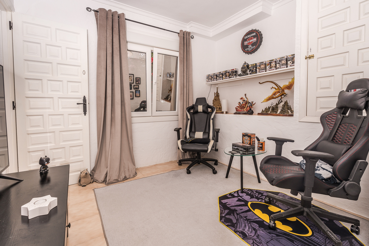 Modern hobby room featuring two ergonomic gaming chairs, white paneled doors, and built-in shelving. Includes double-glazed windows and tiled flooring.