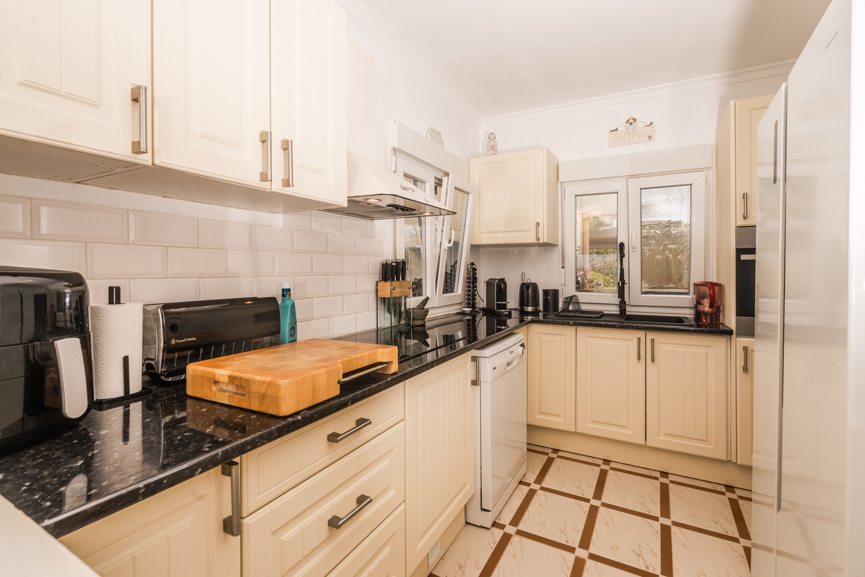 Modern kitchen featuring cream shaker cabinetry, black granite countertops, and white subway tiles. The space includes integrated appliances and a decorative geometric tiled floor.