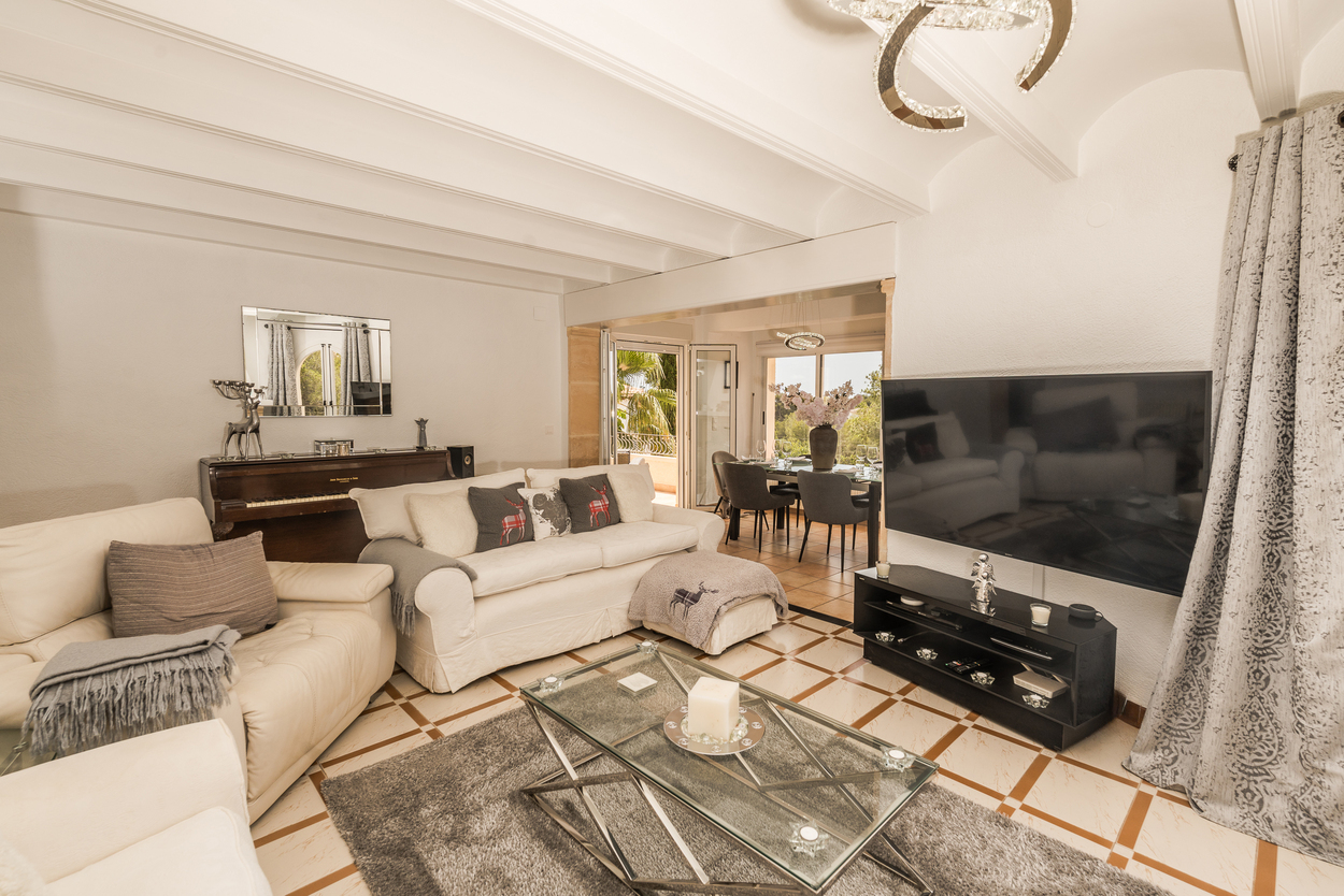 Spacious living area featuring white beamed ceilings, a traditional tosca stone archway, and tiled floors. The room connects to a bright dining space and outdoor terrace.
