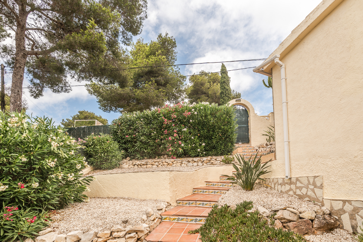 Terraced Mediterranean garden featuring terracotta steps with decorative tiles, gravel landscaping, and mature oleander bushes leading to an arched gate.