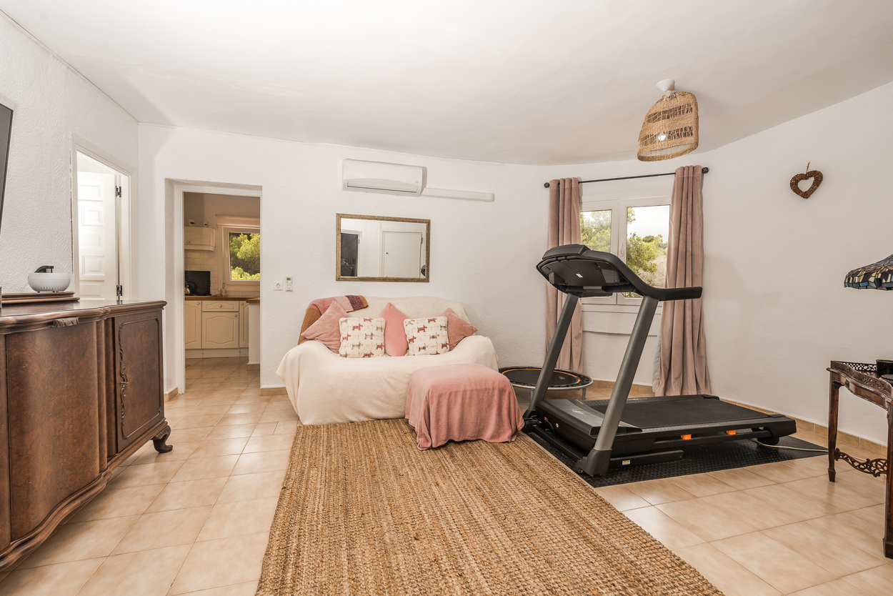 Versatile living area featuring a fitness zone with a treadmill, tiled flooring, and air conditioning, providing access to the kitchen.