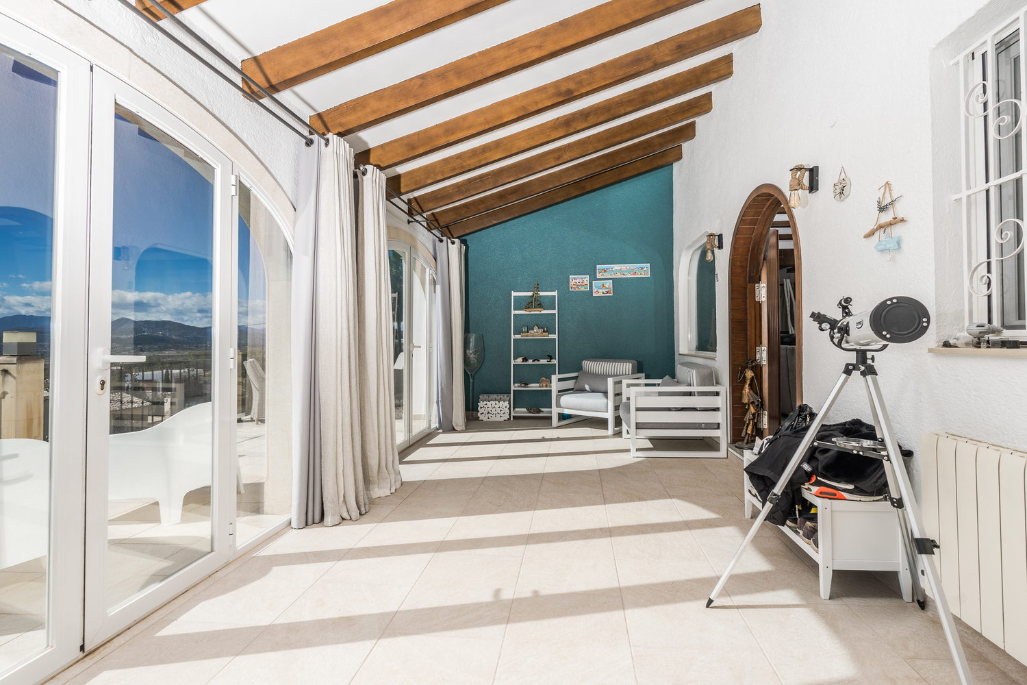 Glazed naya featuring exposed wooden ceiling beams, tiled flooring, and large glass doors opening to panoramic mountain views and natural light.