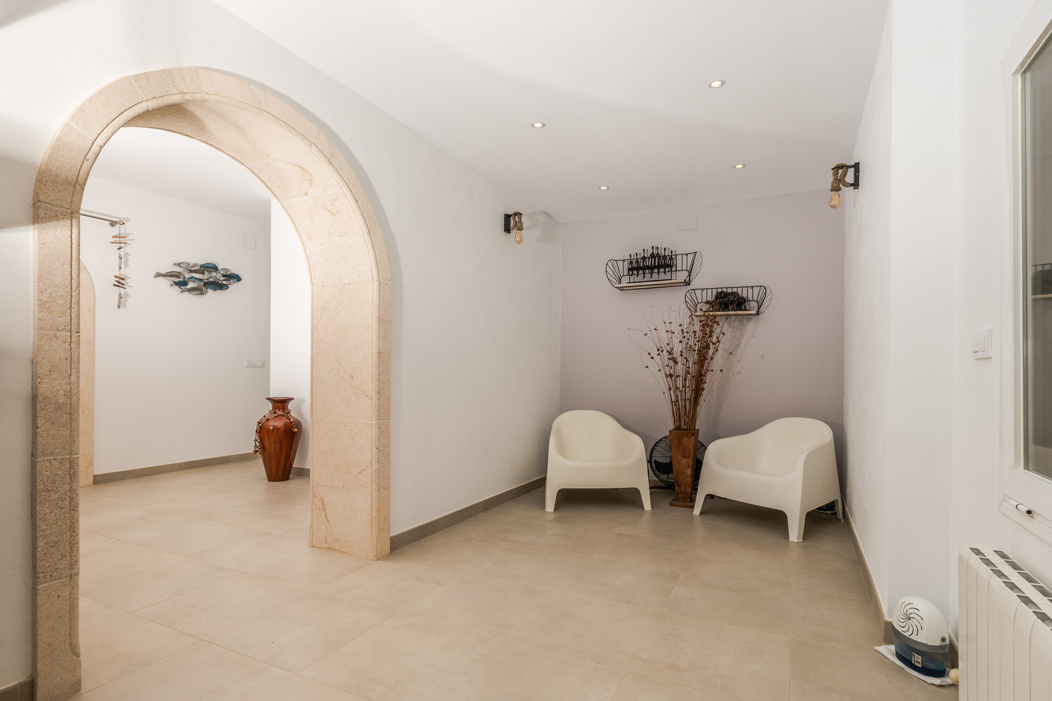 Hallway featuring a traditional Tosca stone arch, recessed ceiling lights, and a minimalist seating area with modern white armchairs and industrial wall sconces.