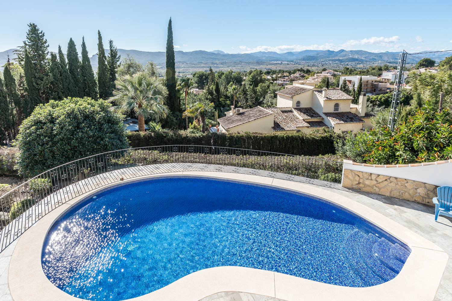Kidney-shaped swimming pool with blue mosaic tiling, surrounded by a stone terrace and wrought iron railing, overlooking the valley and mountains.