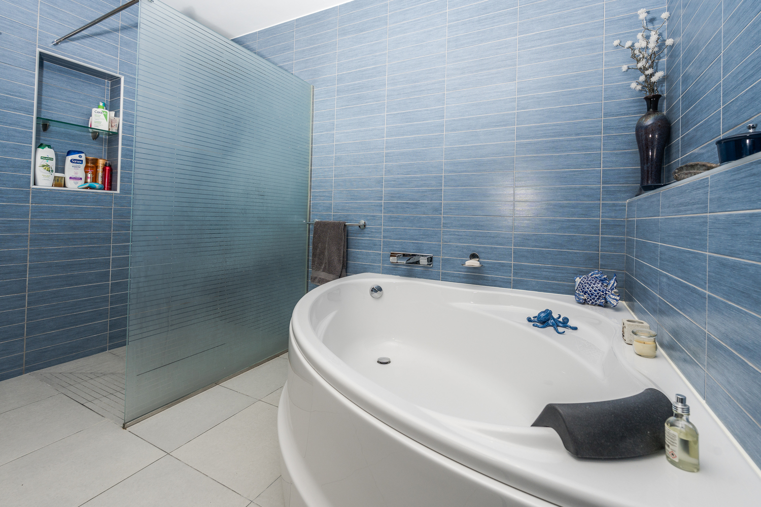 Modern bathroom featuring a large oval bathtub and a walk-in shower with a frosted glass screen, complemented by blue textured wall tiles and light grey flooring.