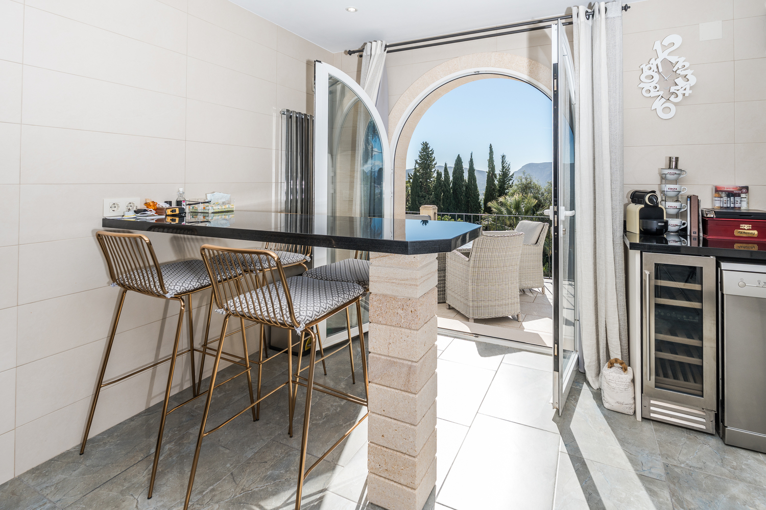 Modern kitchen breakfast bar with black granite surface and gold stools, opening through a stone arch to a terrace with valley and mountain views.