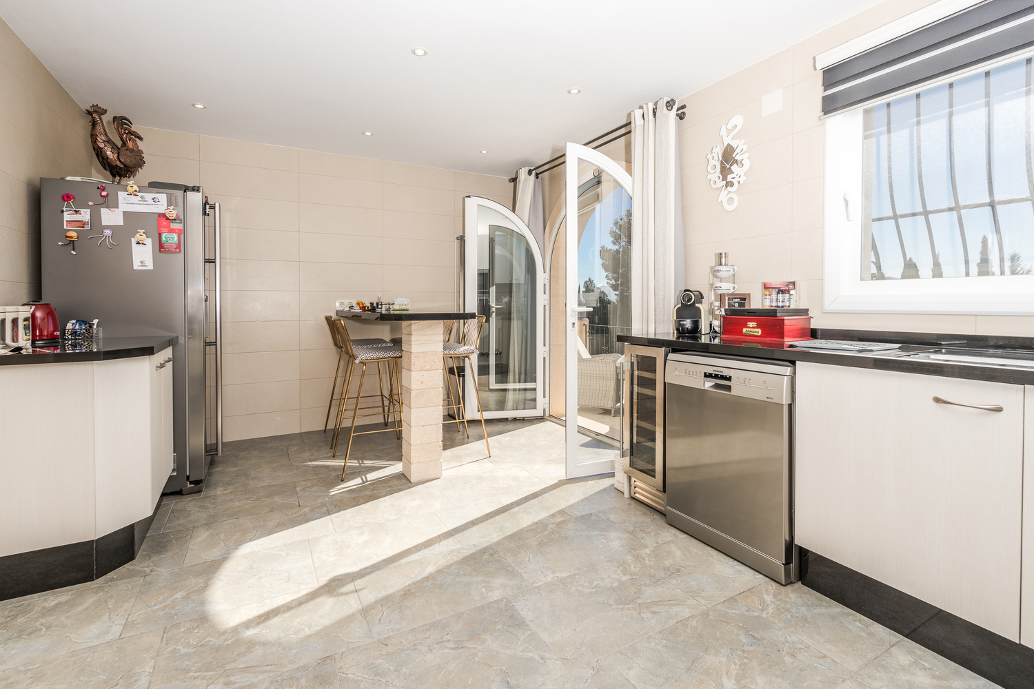 Modern kitchen featuring white cabinetry, black granite countertops, and a breakfast bar. Includes stainless steel appliances and an arched glass door leading to the terrace.