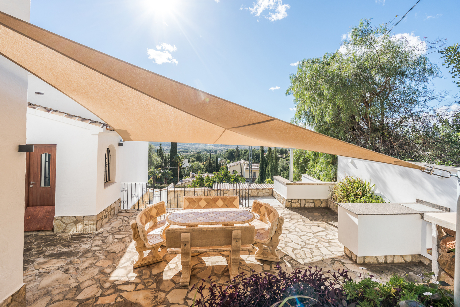 Outdoor terrace featuring a stone dining set under a large shade sail, providing panoramic valley views and access to the summer kitchen.