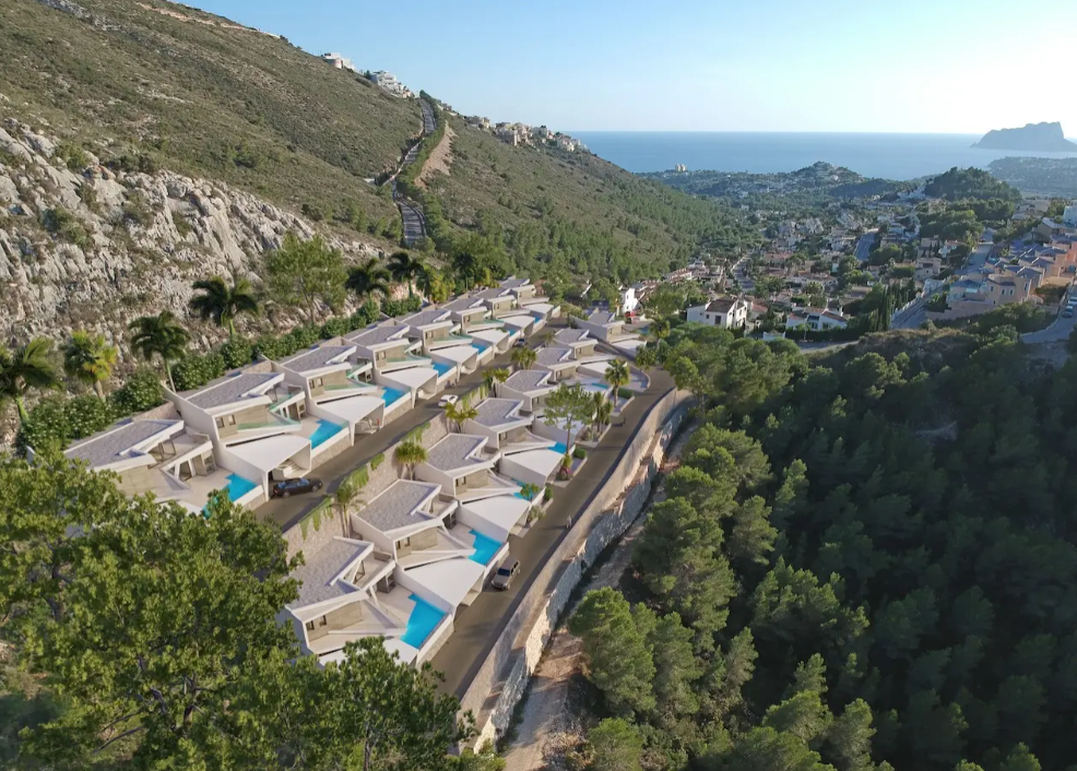 Aerial perspective of sixteen modern villas tiered on a Benitachell hillside, each featuring a private turquoise pool and views of the Mediterranean coastline.
