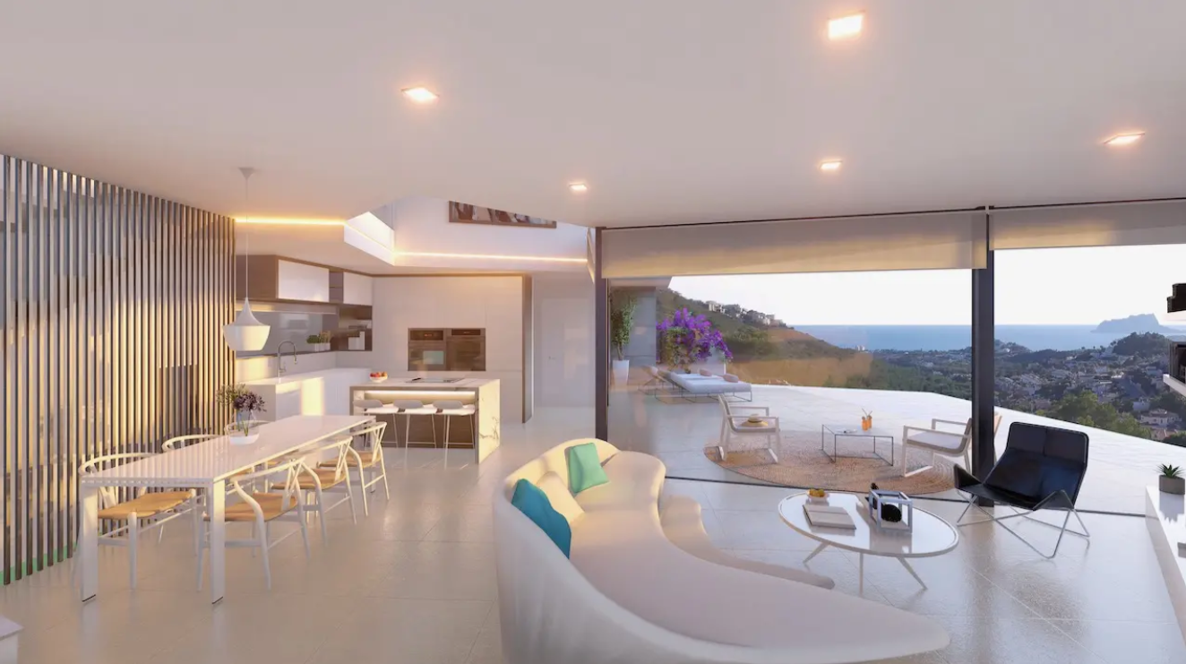 Open-plan living space featuring curved seating, a dining suite, and an integrated kitchen. Floor-to-ceiling glass doors open onto a terrace overlooking the Mediterranean coastline.