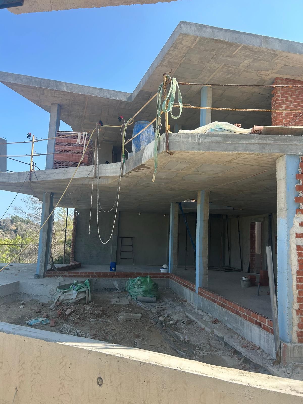Structural phase of a multi-level villa in Benitachell, featuring reinforced concrete slabs, pillars, and initial brickwork.