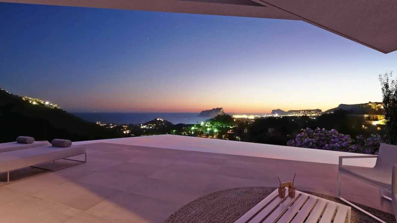 Terrace with infinity pool and panoramic views of the Mediterranean coast at dusk. Features large-format tiling, modern outdoor furniture, and views of the Peñón de Ifach.