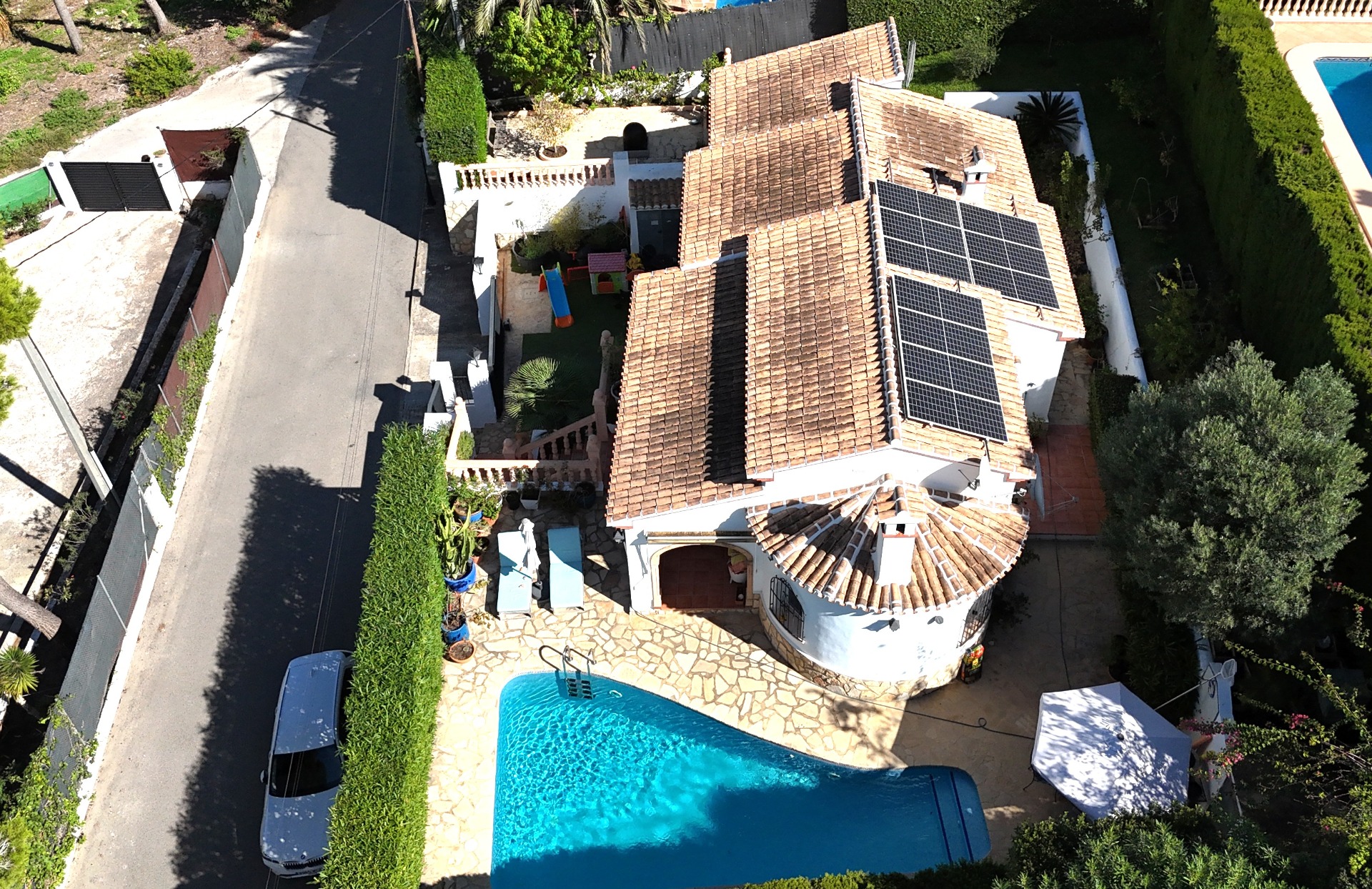 Aerial view of the villa featuring a private pool, solar panel installation on the terracotta roof, and a dedicated children's play area within the gated plot.