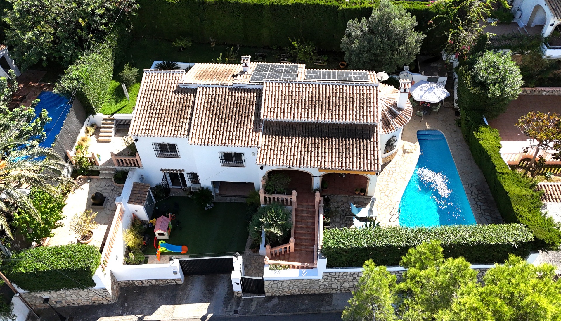 Aerial view of this Toscal villa featuring a terracotta roof with solar panels, a private swimming pool, and a dedicated children's play area within landscaped gardens.