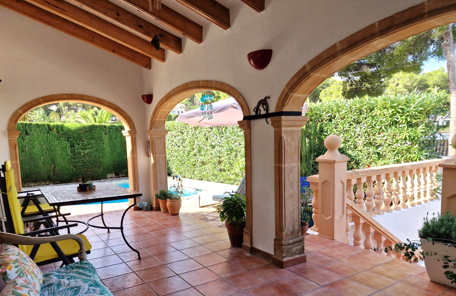 Covered terrace featuring traditional Tosca stone arches, exposed wooden beams, and terracotta tiling, overlooking the private pool and garden area.