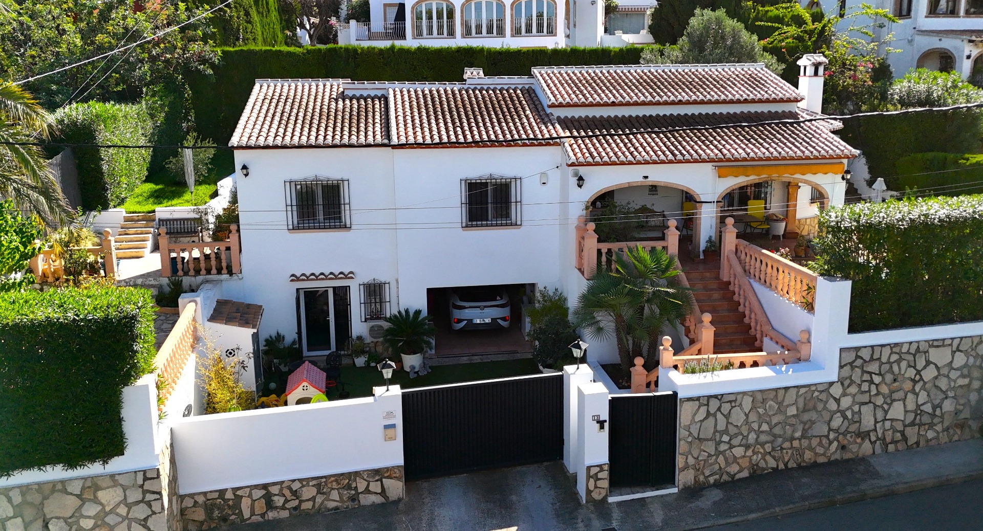 Exterior view of a two-level Mediterranean villa featuring a white facade, terracotta roof, integrated garage, and arched terrace with stone balustrades.