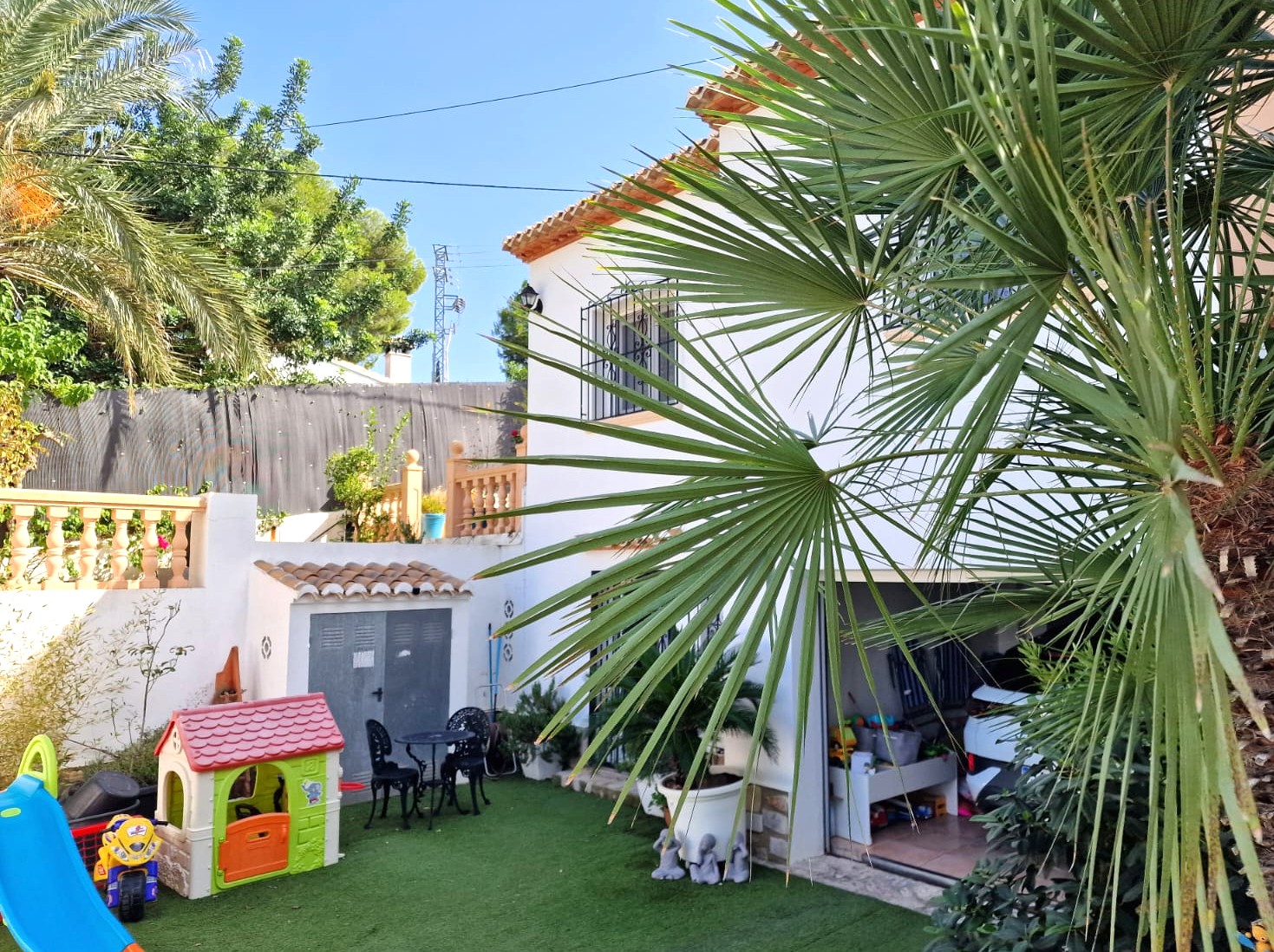 Exterior view showing the lower level with a children's play area on artificial turf, a separate storage shed, and the entrance to the open garage.