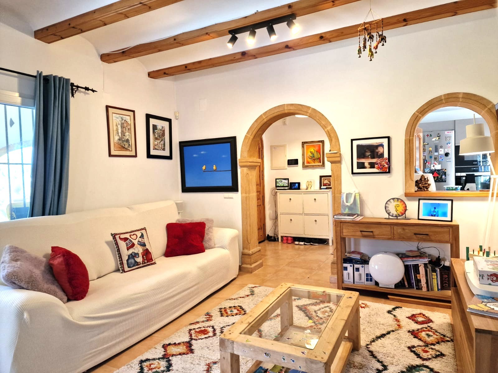 Living area featuring traditional exposed wooden beams, Tosca stone arches, and a bright layout connecting to the kitchen through an arched opening.