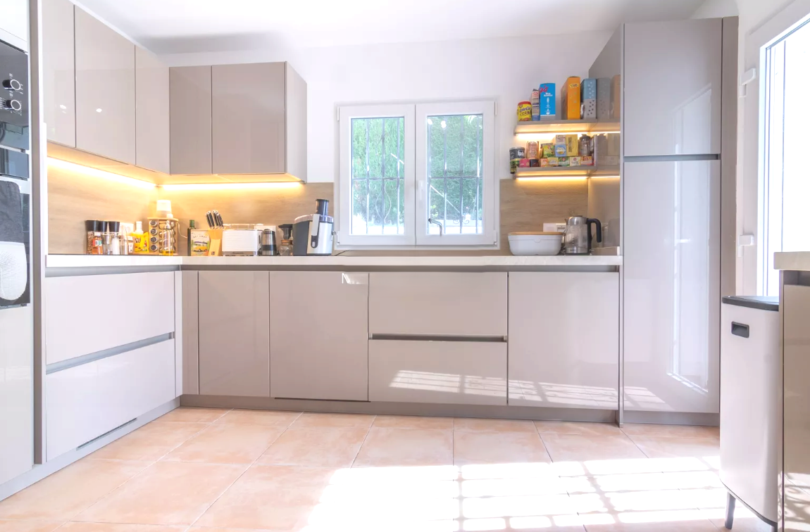Modern kitchen featuring high-gloss taupe cabinetry, white countertops, and integrated LED lighting. Includes built-in appliances and terracotta-style tile flooring.