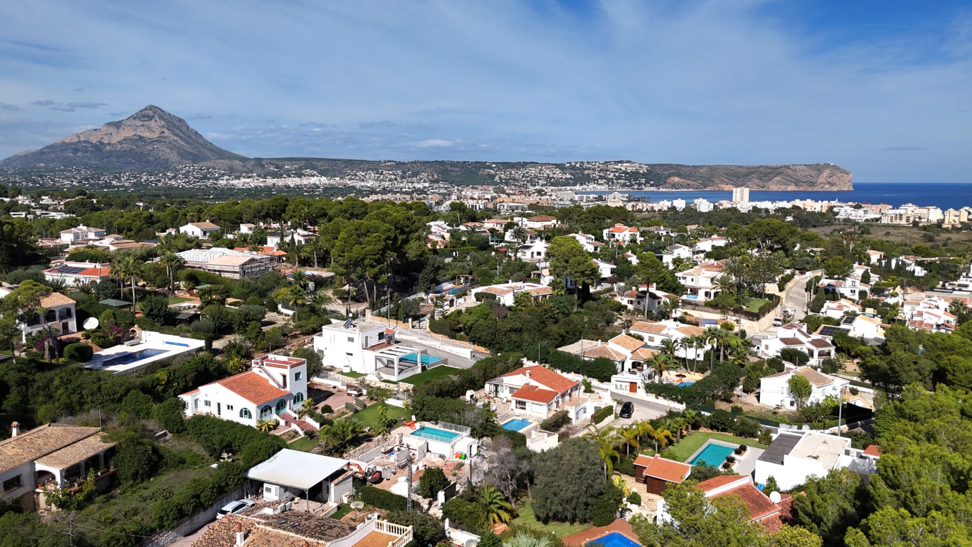 Panoramic aerial view of the Toscal area in Jávea, showcasing the Montgó mountain, Cabo San Antonio, and the Mediterranean coastline under a clear sky.
