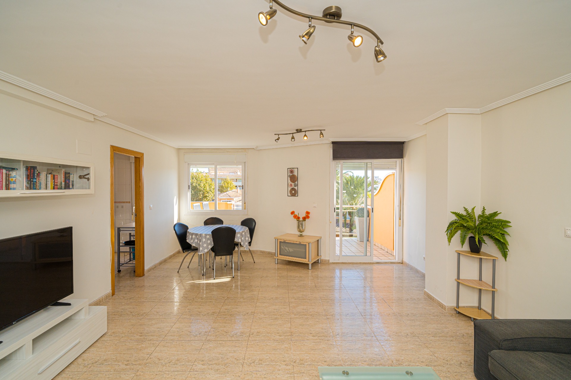Spacious living and dining area featuring polished tile floors, track lighting, and direct access to a private terrace through sliding glass doors.