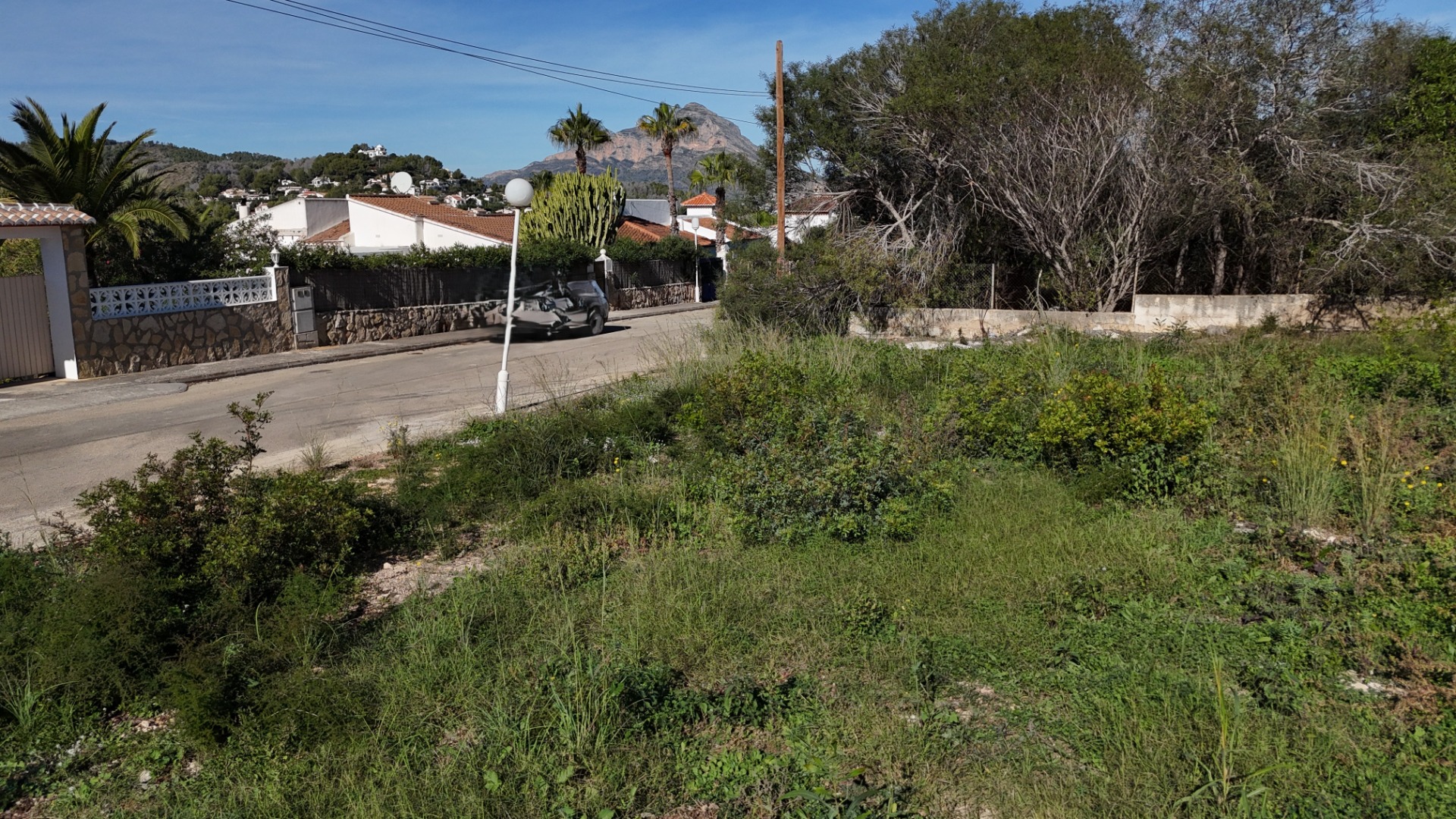 Flat building plot in Pinosol, Jávea, featuring direct street access and clear views of the Montgó mountain across a quiet residential road.