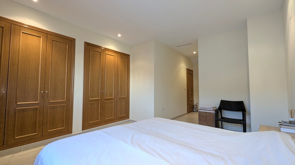 Bedroom featuring extensive built-in wooden wardrobes, recessed ceiling lighting, and neutral-toned tiled flooring.