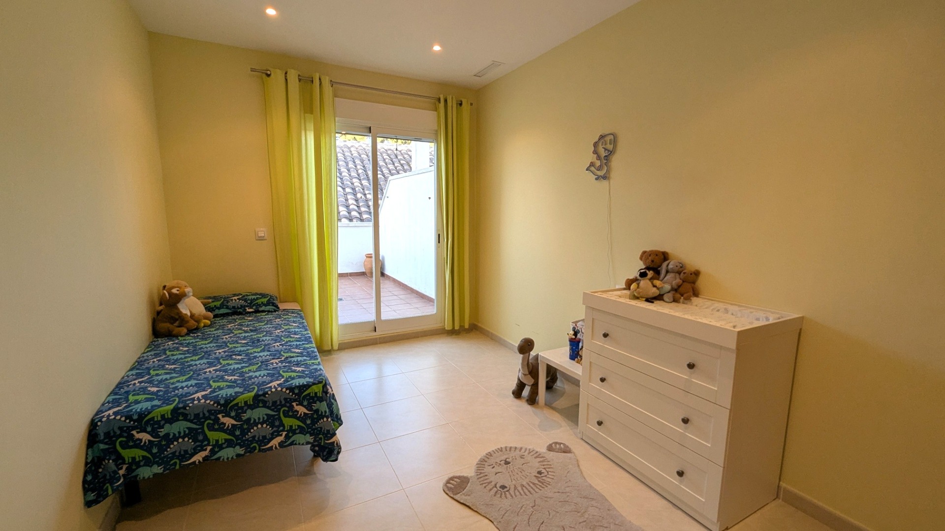 Bright bedroom featuring tiled flooring, lime green curtains, and a sliding glass door providing direct access to a private outdoor terrace.
