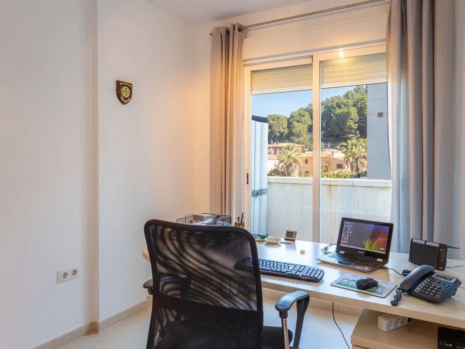 Bright home office space featuring a large desk and ergonomic chair, with sliding glass doors opening to views of the wooded hills in Jesús Pobre.