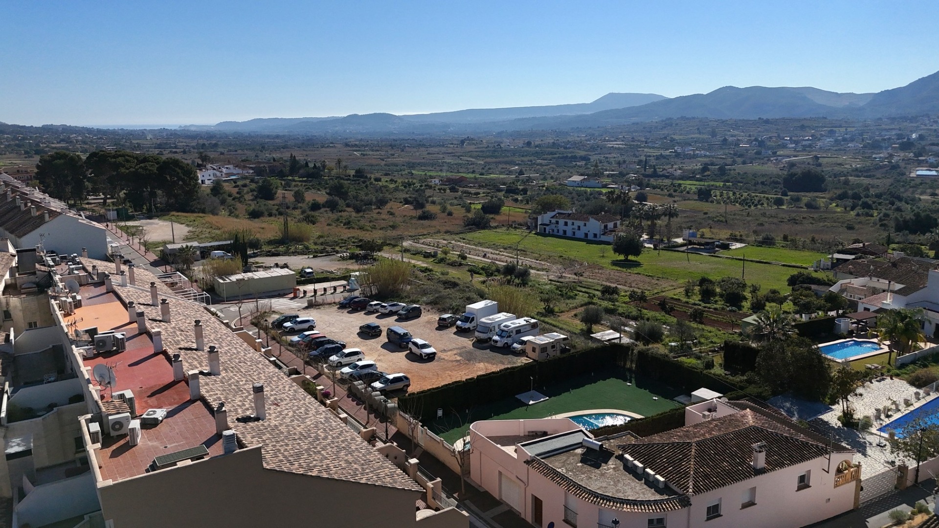 Elevated view from the penthouse overlooking the communal pool, parking area, and the expansive countryside towards the distant mountains.