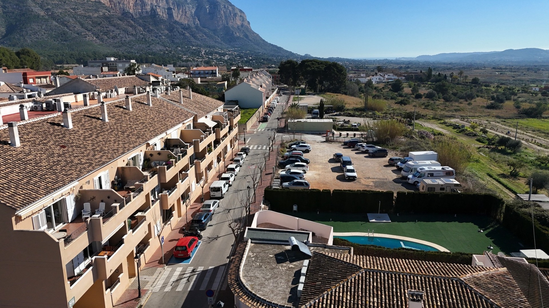Elevated view of the residential complex featuring the communal pool, street parking, and panoramic vistas of the Montgó mountain and surrounding countryside.