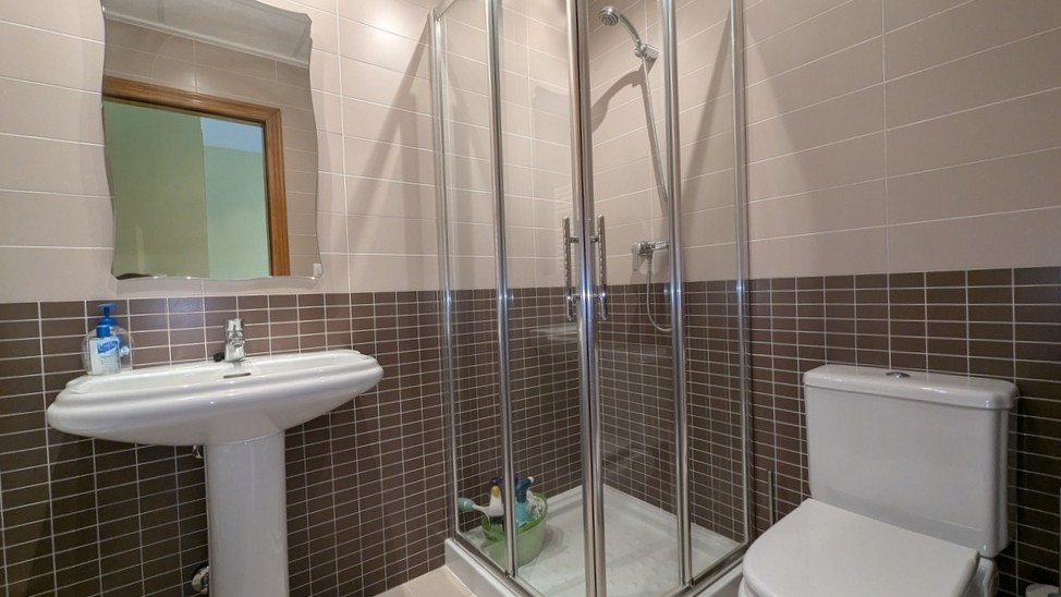 Functional bathroom featuring a corner glass shower enclosure, pedestal sink, and two-tone wall tiling in brown and beige.