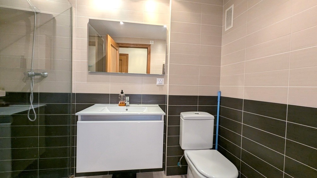 Modern bathroom featuring two-tone wall tiles, a white floating vanity, rectangular mirror, and walk-in shower with glass partition.