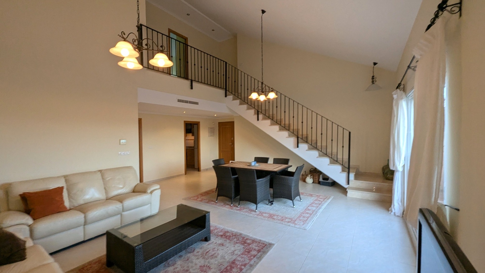 Spacious living and dining area featuring high ceilings, a staircase with wrought-iron railings, and a mezzanine level overlooking the main floor.