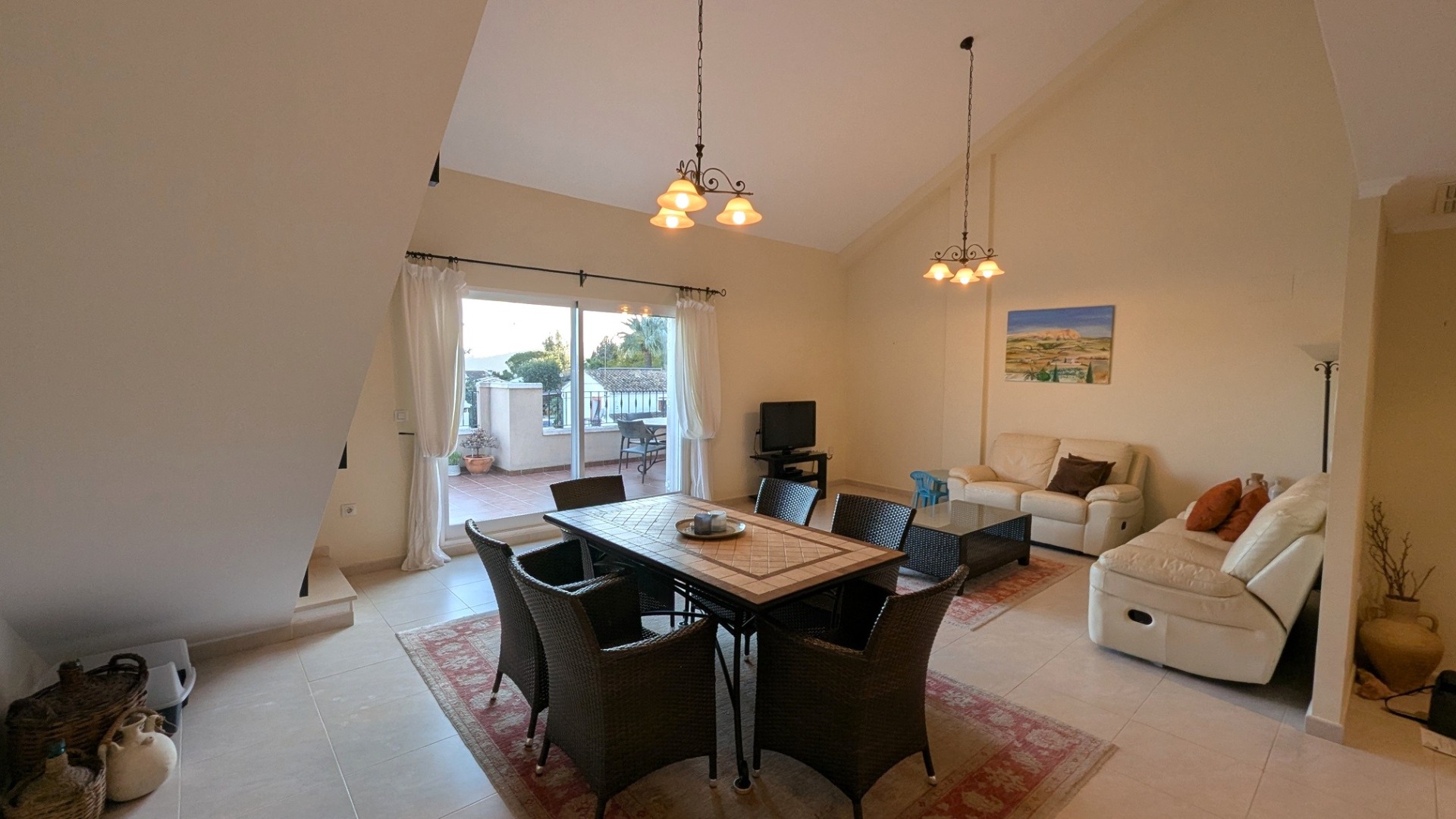 Spacious living-dining area featuring high vaulted ceilings, tiled flooring, and sliding glass doors opening onto a private terrace with outdoor seating.